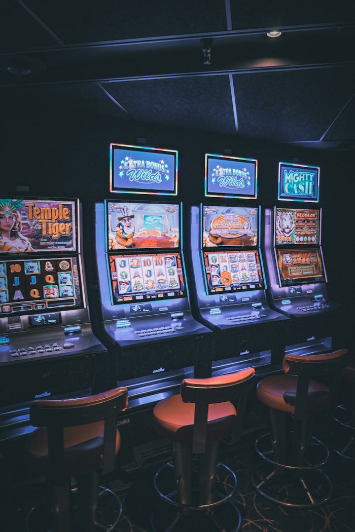 Row of illuminated slot machines in a dimly lit, empty casino area.