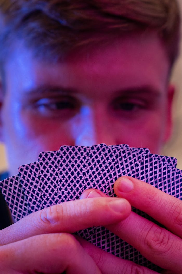 Close-up of a man intently holding playing cards under soft purple lighting.